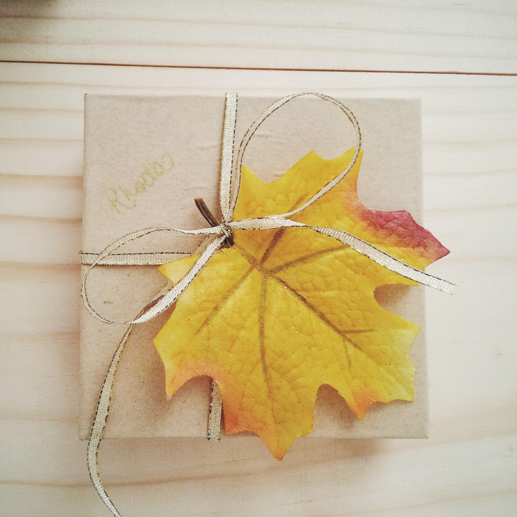 Small brown paper box tied with gold ribbon and golden yellow leaf on top