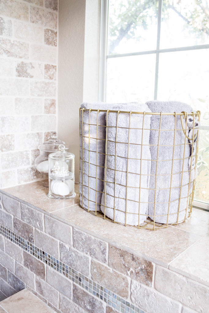 glass apothecary jars and gold basket with grey towels in master bathroom