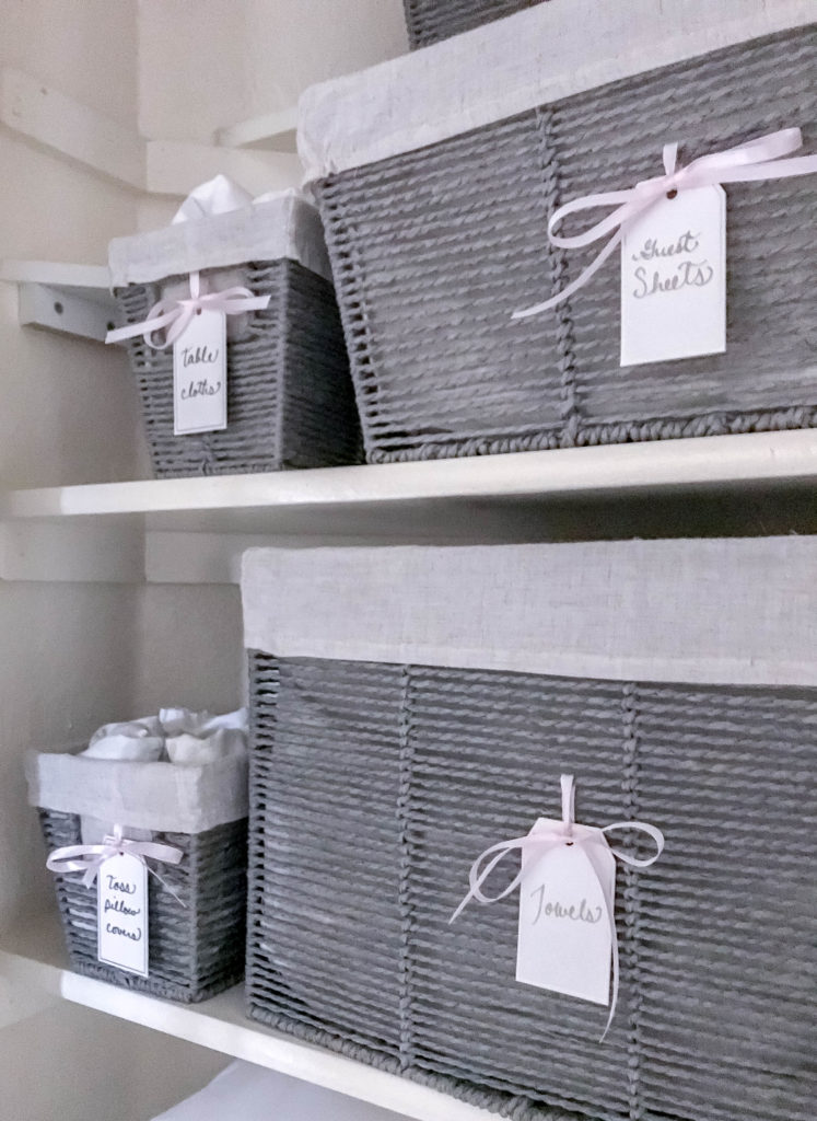 grey baskets with tags and pink ribbons inside linen closet