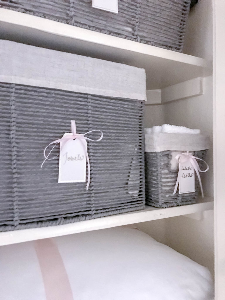 grey baskets with tags and pink ribbons in linen closet
