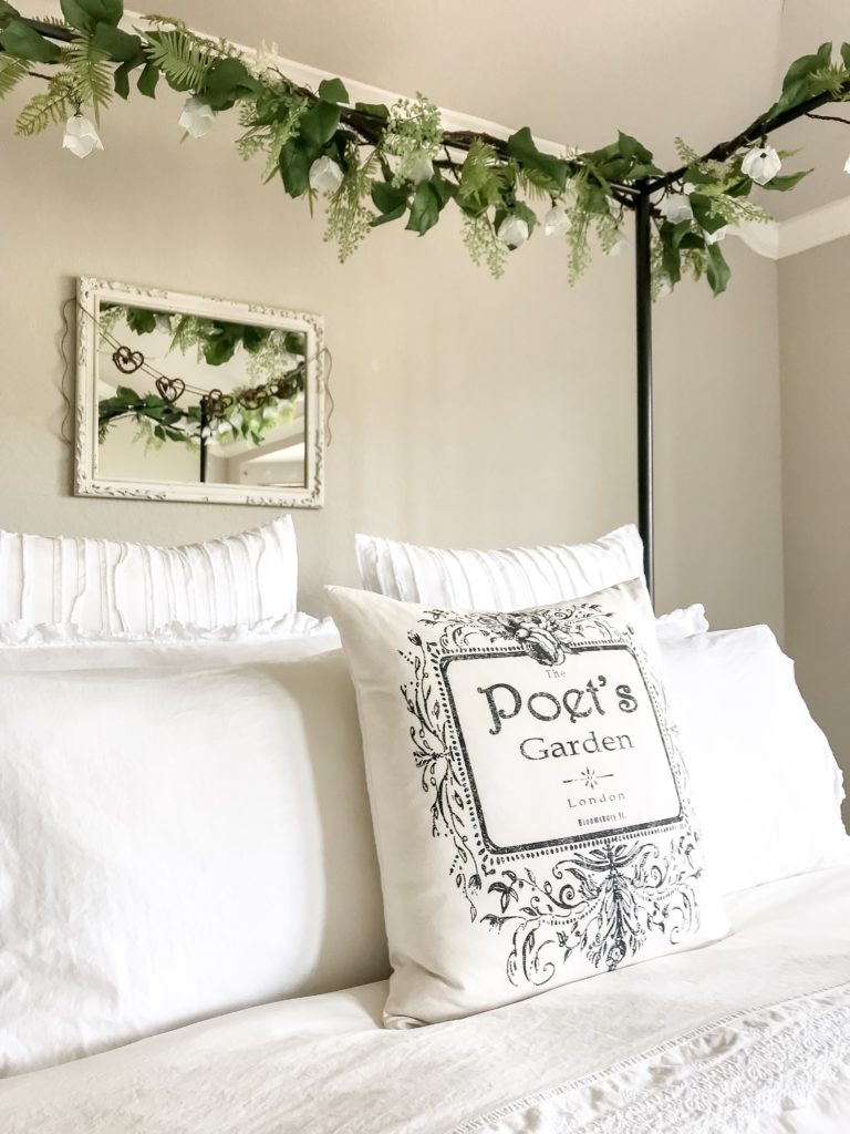 toss pillow that says poet's garden, white mirror with heart garland and green garlands at top of canopy bed