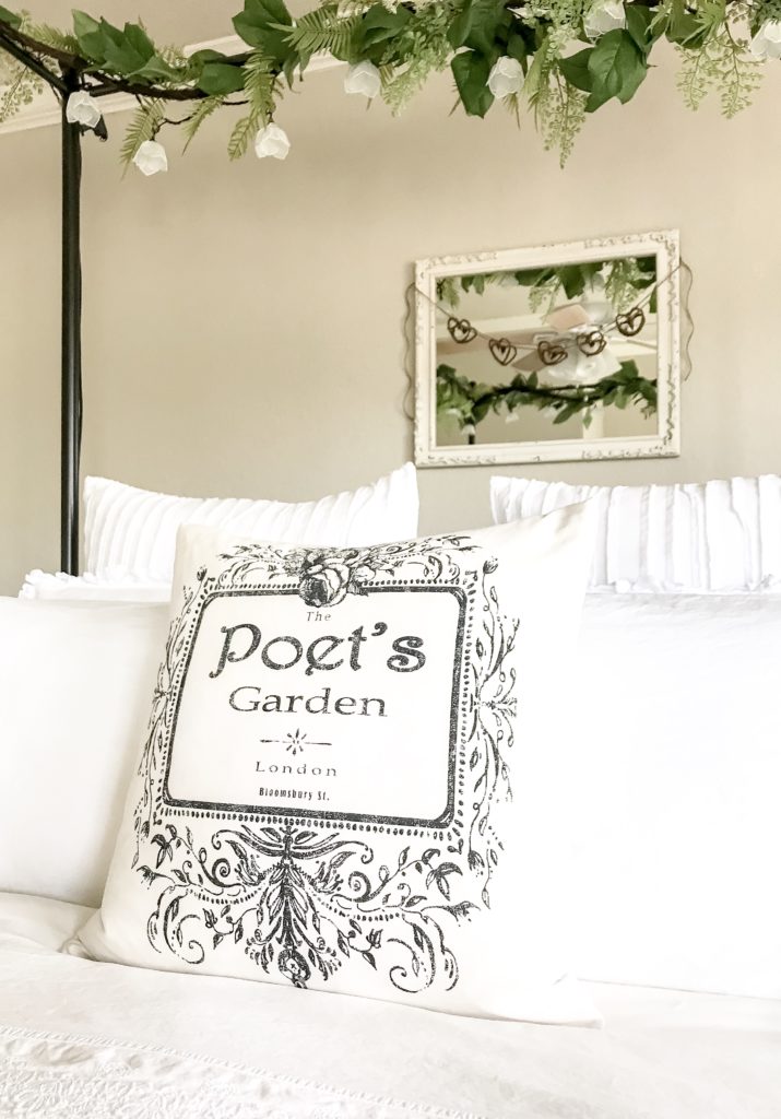 view of front of bed with pillow that says poet's garden and white mirror with heart garland