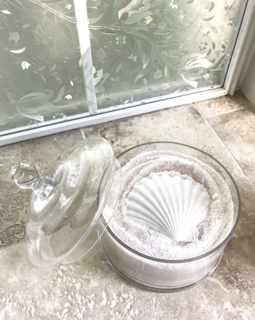 pink bath salts in glass jar with white seashell as scooper on top