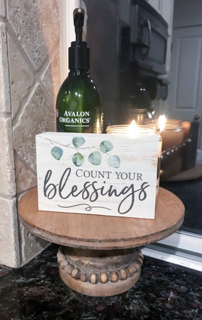 Candle burning on stand by sink with lotion and decorative sign