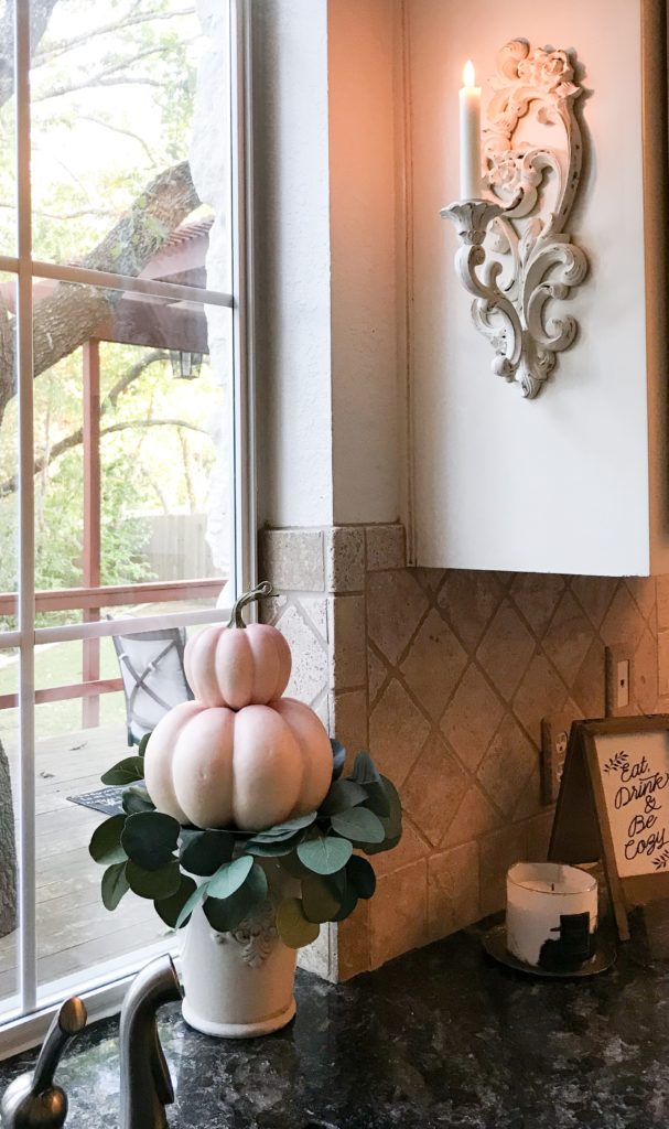 candle lit in candle sconce on cupboard and pumpkin topiary underneath 