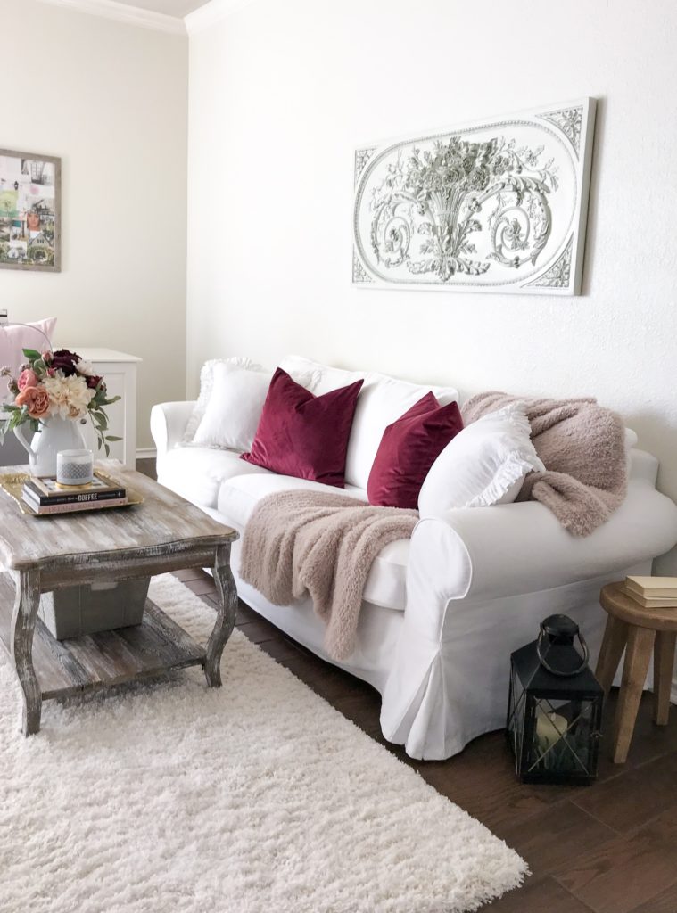 white couch with pink blanket and berry pillows under a french wall art piece